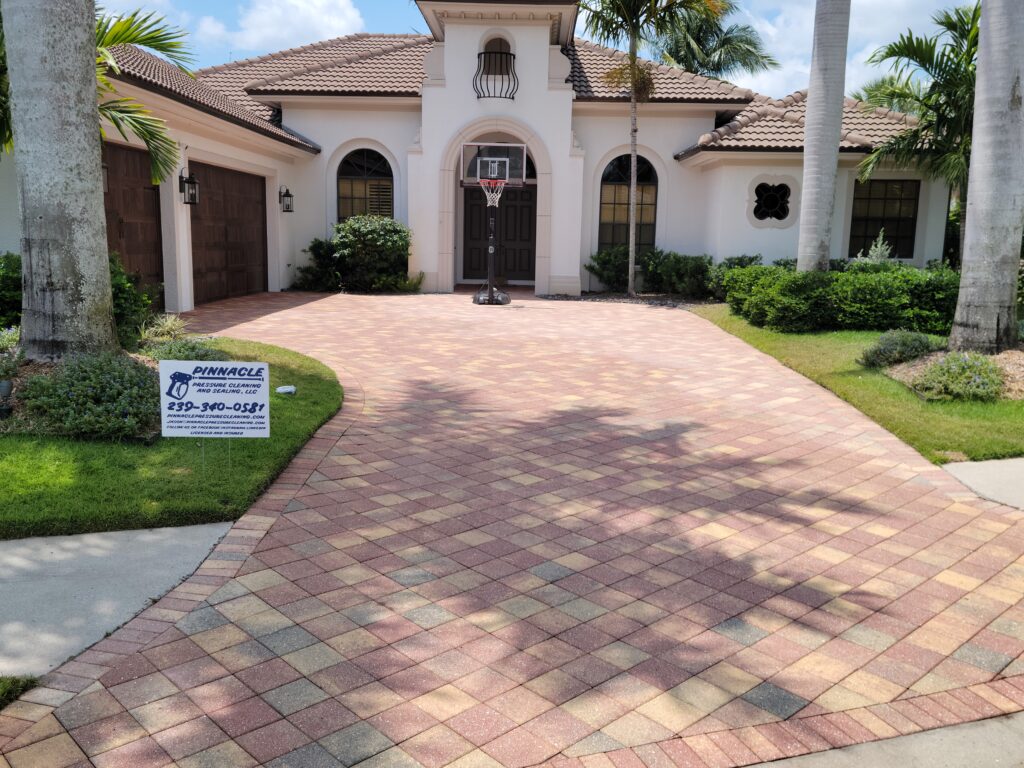 Elegant home in Naples with a driveway freshly cleaned by Pinnacle Pressure Cleaning and Sealing, showcasing their Naples pressure cleaning services, with a company sign visible on the lawn.