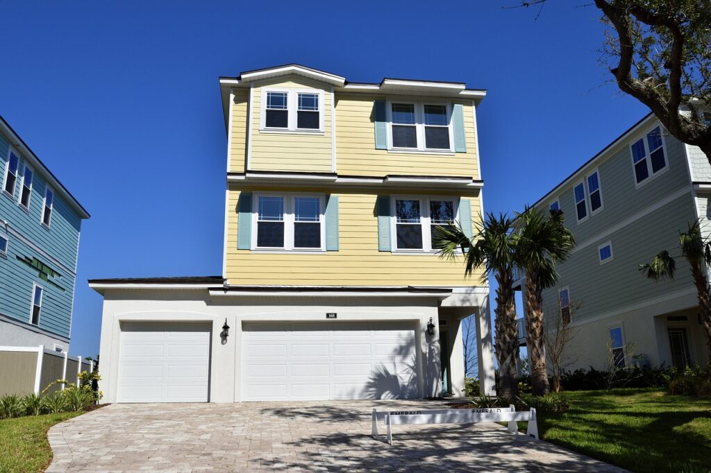 A three-story yellow house with a clean driveway and exterior, serviced by Pinnacle Pressure Cleaning and Sealing, under a bright blue sky in Naples.